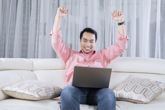 Cheerful male raising hands with a laptop