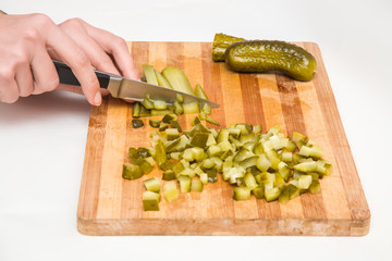 Woman's hands on the wooden board with a knife cutting a pickled cucumber for salad. Healthy eating and lifestyle.