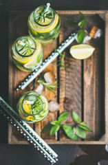 Citrus and herbs infused sassi water for healthy eating, dieting in glass bottles in wooden tray over dark background, selective focus, top view, copy space. Clean eating, healthy lifestyle concept
