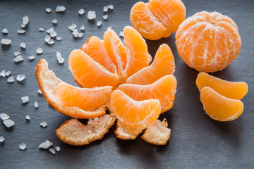Pieces of mandarin with peels. Composition of tangerines on the dark background.