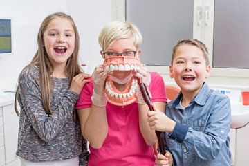 Junge Zahnarzthelferin zeigt zwei Kindern spielerisch das richti