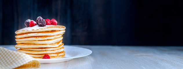 Pancake on a white plate with fruit and powdered sugar on a wooden background