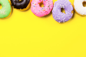 Pink round donut and few other on yellow background. Flat lay, top view.