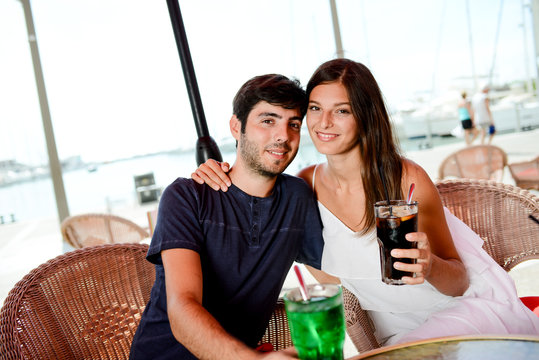 cheerful young couple having drinks at terrace of seaside walk tourist resort harbor