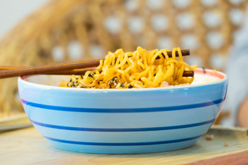 Instant Noodles in Ceramic Bowl with Chopstick and Rattan Backgr