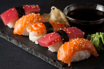Sashimi and sushi rolls on a stone slatter. Sushi set with salmon, prawns, soy souce, wasabi and ginger. Traditional Japanese cuisine.