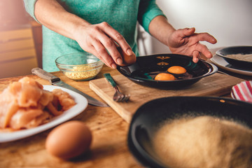 Woman cooking and breaking eggs into the plate