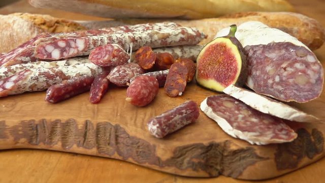 Camera movement near uncooked jerked sausages, baguette and figs on a wooden board