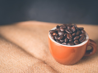Coffee beans in italian espresso cup on burlap and dark blue black background