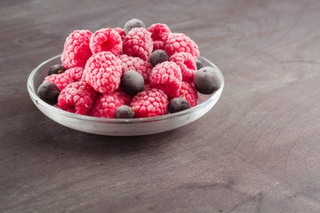 Frozen raspberries in a glass saucer. Frost on the berries. Dark background.