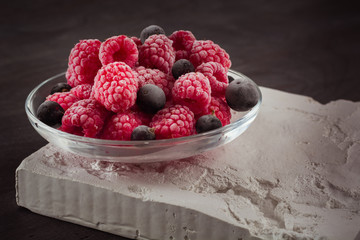 Frozen raspberries in a glass saucer. Frost on the berries. Dark background.