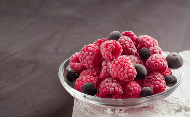 Frozen raspberries in a glass saucer. Frost on the berries. Dark background.