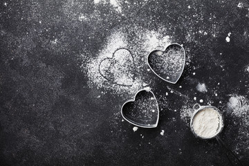 Baking background with flour and heart shape on kitchen black table top view for Valentines day cooking. Flat lay style.