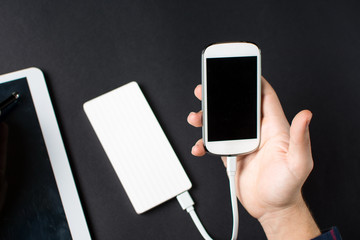 male hands holding a white cellphone connected to a power bank