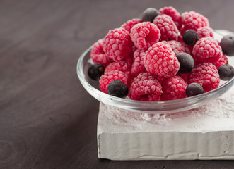Frozen raspberries in a glass saucer. Frost on the berries. Dark background.