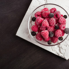 Frozen raspberries in a glass saucer. Frost on the berries. Dark background.