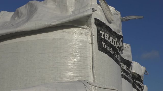 Row of bulk bags containing loose building material against blue sky, low angle