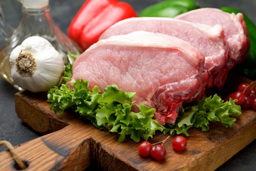 raw pork steaks, lettuce on a cutting board