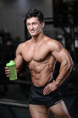 Fototapeta na wymiar Handsome fitness model holding a shaker in the gym gain muscle.