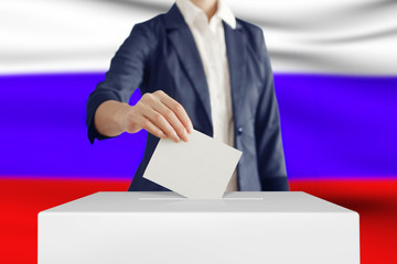 Voting. Woman putting a ballot into a voting box with Russian flag on background.