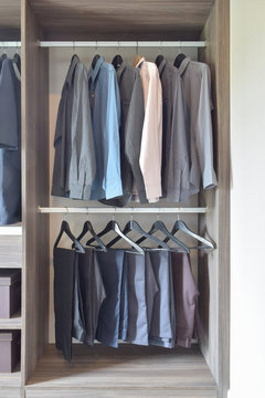 row of colorful shirts and pants hanging  in wooden wardrobe