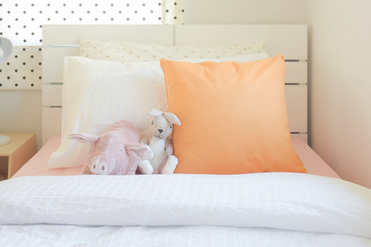Piggy and rabbit doll setting on bed next to orange color pillow in cutie style bedroom 