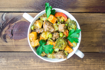 Beef meat stewed with vegetables in ceramic pot on wooden background