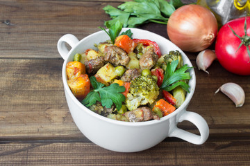 beef meat stewed with vegetables in ceramic pot with ingredients on wooden background
