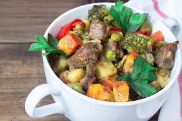 closeup beef meat stewed with vegetables in ceramic pot on wooden background