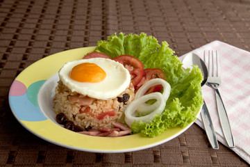 Fry rice with ham , tomato , onion , raisin and egg on top.