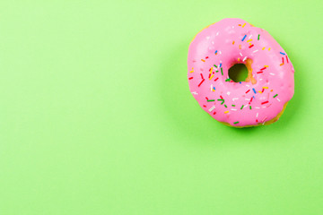 Pink round donut on green background. Flat lay, top view.