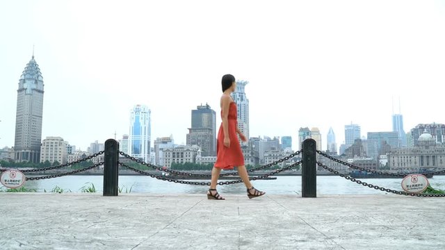 Shanghai woman walking in Pudong by huangpu river with view of the Bund. Tourist or casual girl in beautiful red dress enjoying walk at Pudong boardwalk.