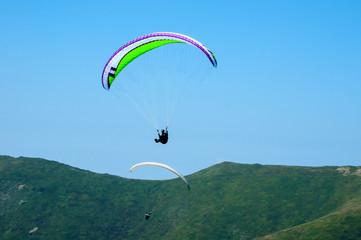Paraglider flies paraglider over the tops of the mountains in summer sunny day. Karpaty, Ukraine.