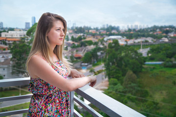 serious young girl looking the city landscape through her balcony