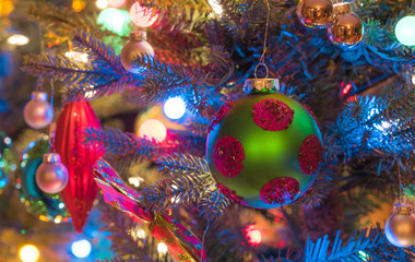 Christmas tree decorations.  Green, matte finish, orb with magenta circles, glows, surrounded by vivid blue and multicolored mini-lights close up on a small faux indoor Christmas tree.
