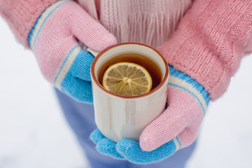 Woman in mittens holding a cup of tea with lemon in winter