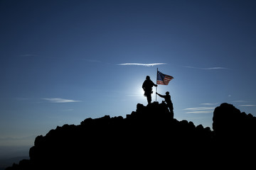 Two soldiers raise the American flag on top of the mountain