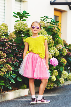 Outdoor portrait of cute little girl wearing green shirt, pink tutu skirt and sunglasses