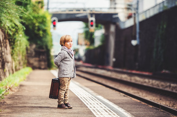 Adorable little boy on a railway station, waiting for the train with suitcase