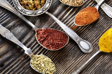 Assortment of spices in vintage spoons on wooden background..
