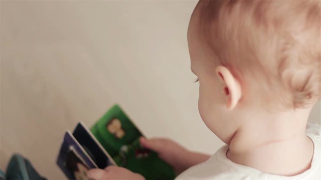 A two year age baby boy sitting on floor in sunny living room and reading a book