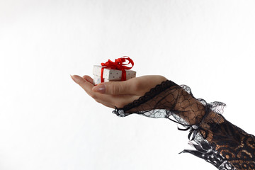 One beautiful female hand in black lace glove holds a gift box with red ribbon