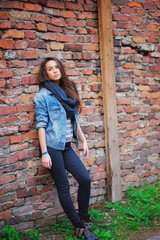 Young pretty girl with long brown hair, dressed in a denim jacket, pants and black scarf looks...