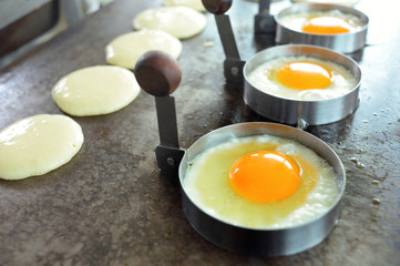 close up fried eggs and pancake on grill pan in individual dishe