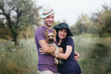 Naklejka na ściany i meble Young couple with little dog yorkshire terrier dressed t-shirt and hat embracing and have fun on the road,travel, vacation, holidays, vacation, love, life style