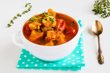 Fish soup with cod, tomato, onion, garlic and thyme in bowl on white table.
