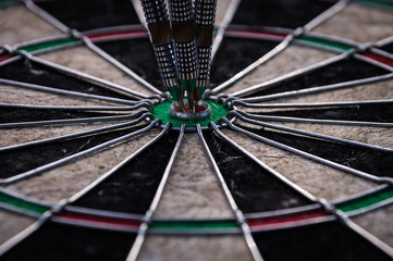 Three dart arrows hitting in the target center of dartboard illustrating the achievement of goals