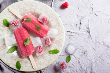 Homemade raspberry popsicles on plate with ice and berries. Summer food concept with copy space for text. Top view.