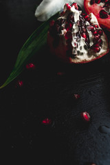 Delicious pomegranate fruit and lilies on black background. Stil