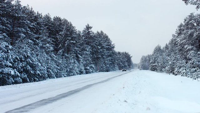 WIDE modern black SUV moving on an empty road towards the camera, forest trees covered with snow in the background. 4K UHD